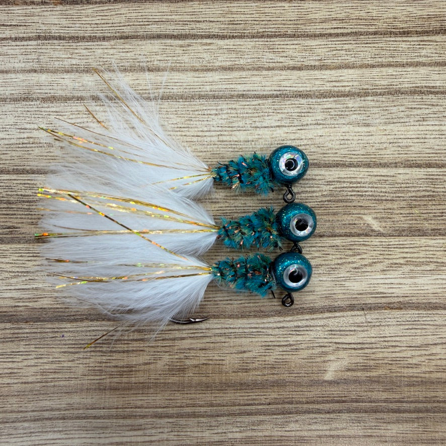 Three crappie fishing jigs with white feathers and blue and green beads on a wooden surface.