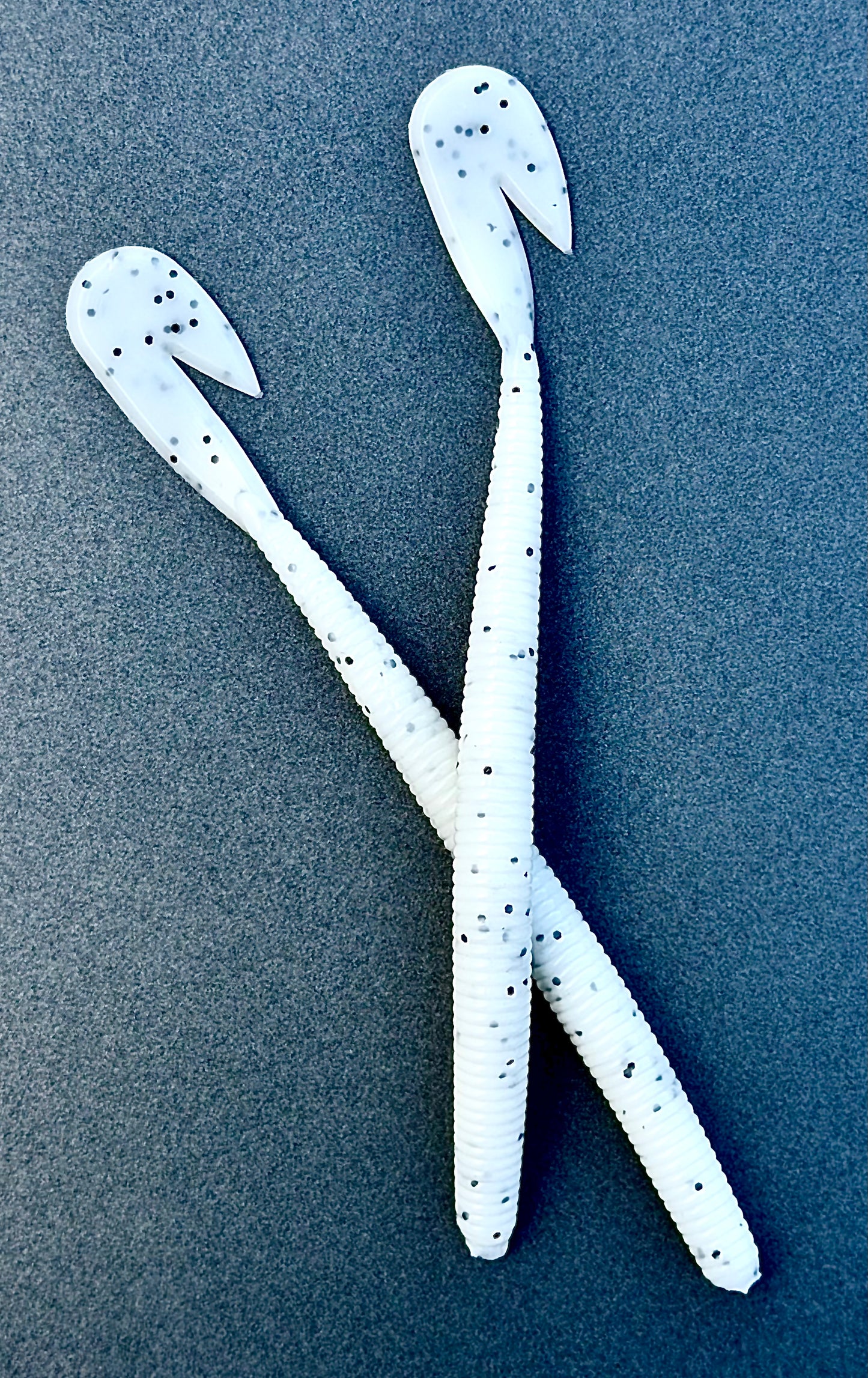 Two white fishing lures with black speckles on a blue textured background