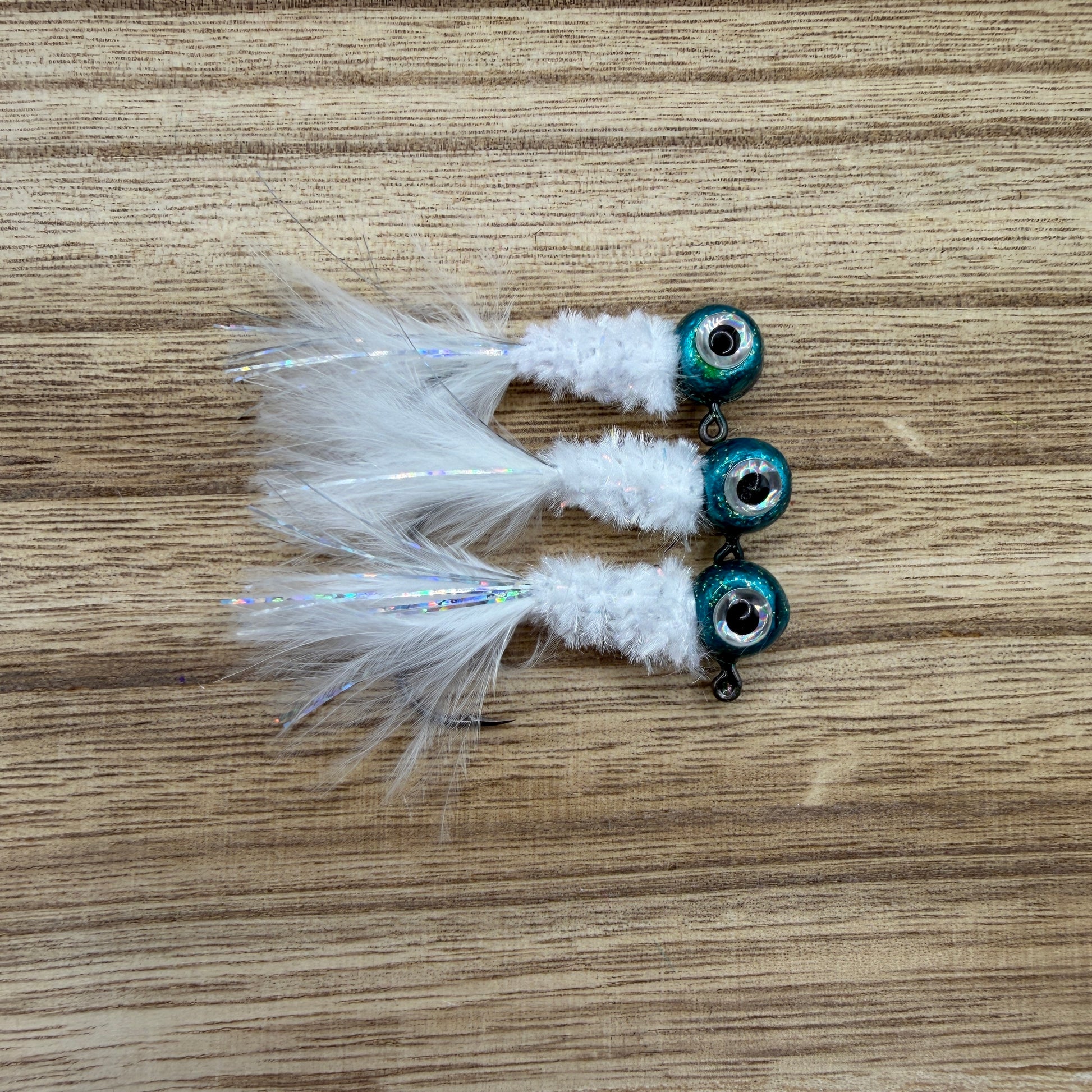 Three crappie fishing jigs with white feathers and blue beads on a wooden surface.
