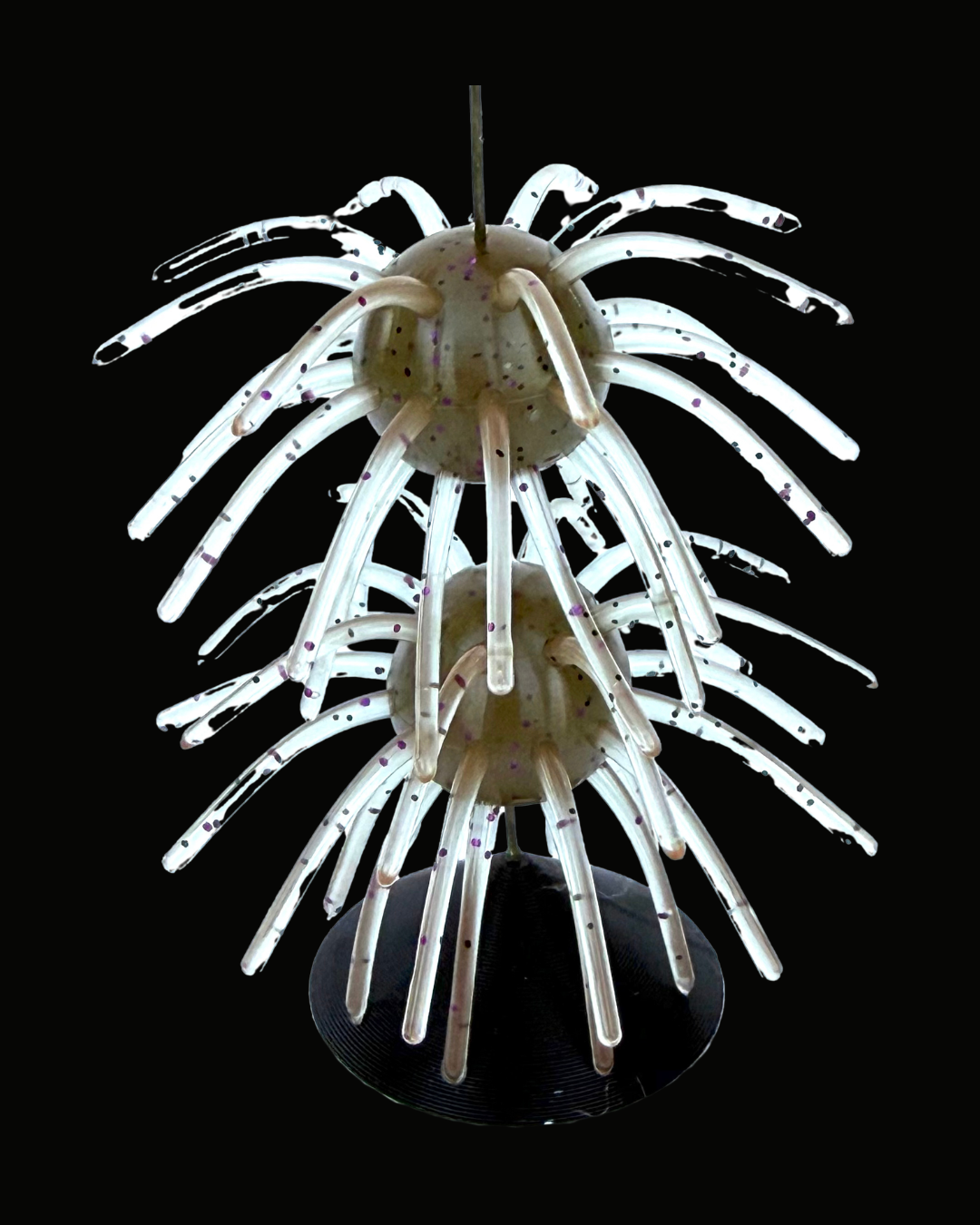 A  fishing lure featuring two translucent white globes with dark speckles, surrounded by numerous radiating glass arms that taper to points, mounted on a black circular base against a solid black background.