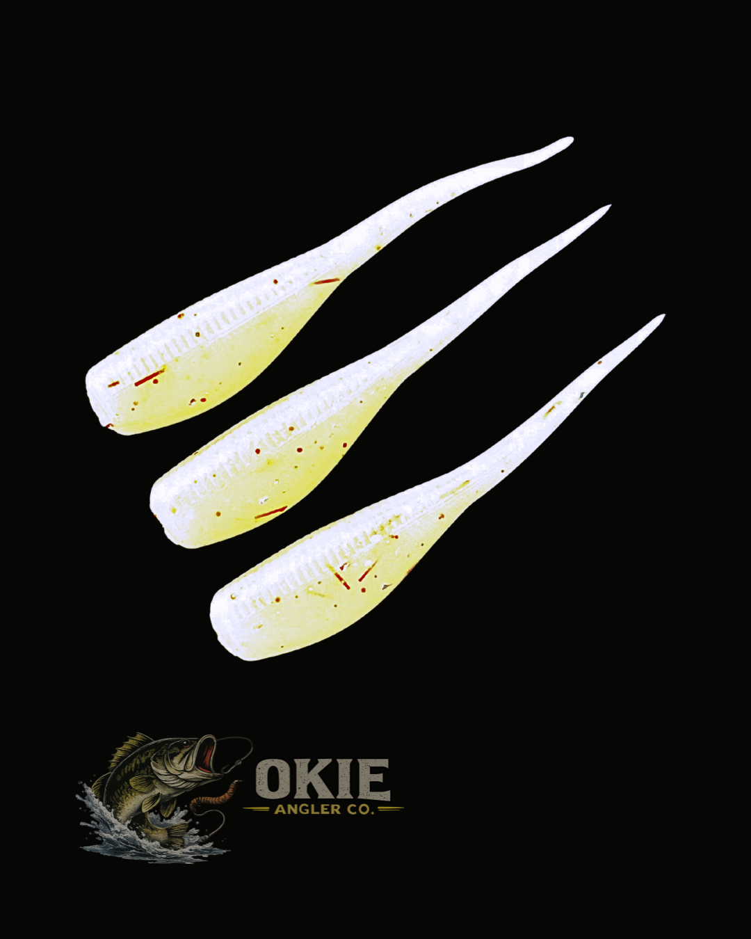 Three soft plastic fishing lures in a translucent pale yellow and white gradient with red and orange flash speckles, arranged diagonally on a black background with the Okie Angler Co. logo at the bottom.