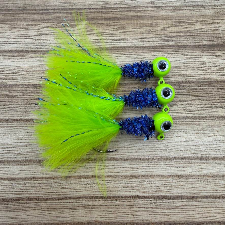 Three crappie fishing jigs with green and blue details on a wooden surface.