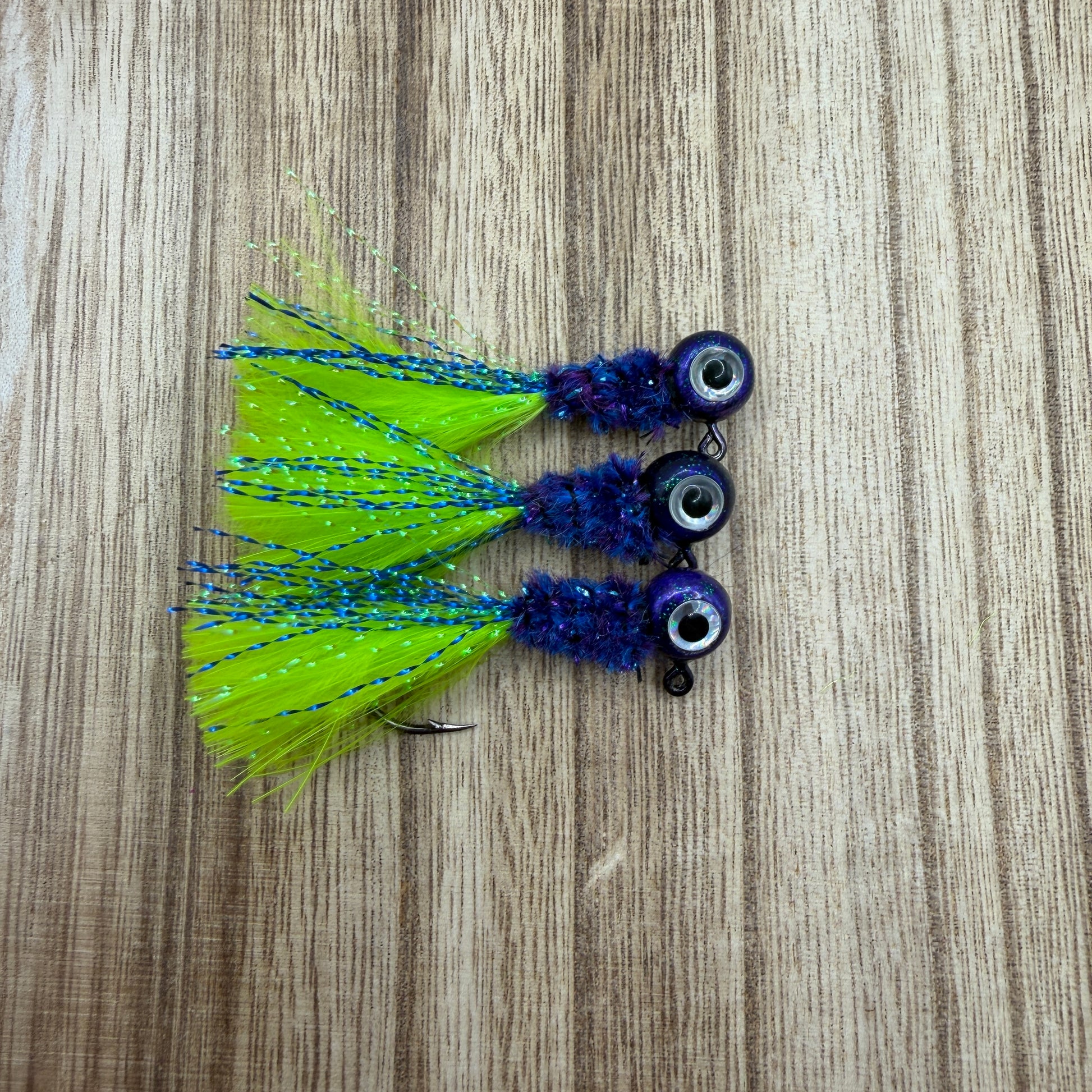 Three crappie fishing jigs with green and blue details on a wooden surface.
