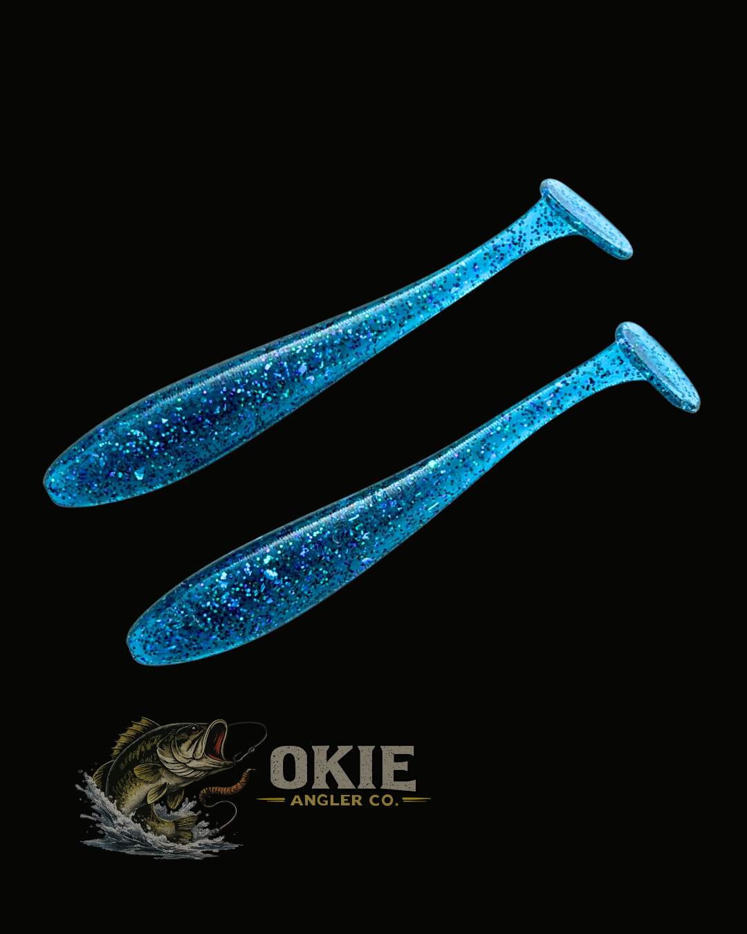 Two blue glitter soft plastic paddle tail fishing lures on a black background, with the Okie Angler Co. logo and fish graphic at the bottom.