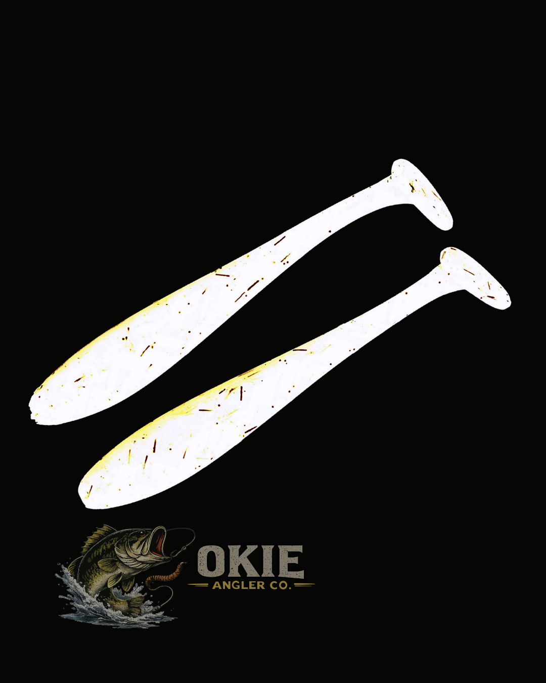 Two white paddle-tail fishing lures with a distressed yellow and brown speckled pattern, displayed on a solid black background with the OKIE Angler Co. logo at the bottom.