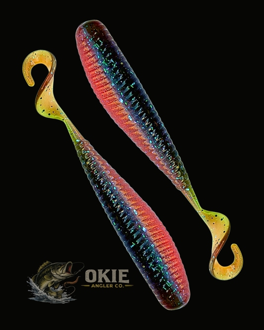 Two soft plastic hook-and-gore fishing lures with a glittery rainbow finish, displayed on a solid black background with the Okie Angler Co. logo at the bottom.