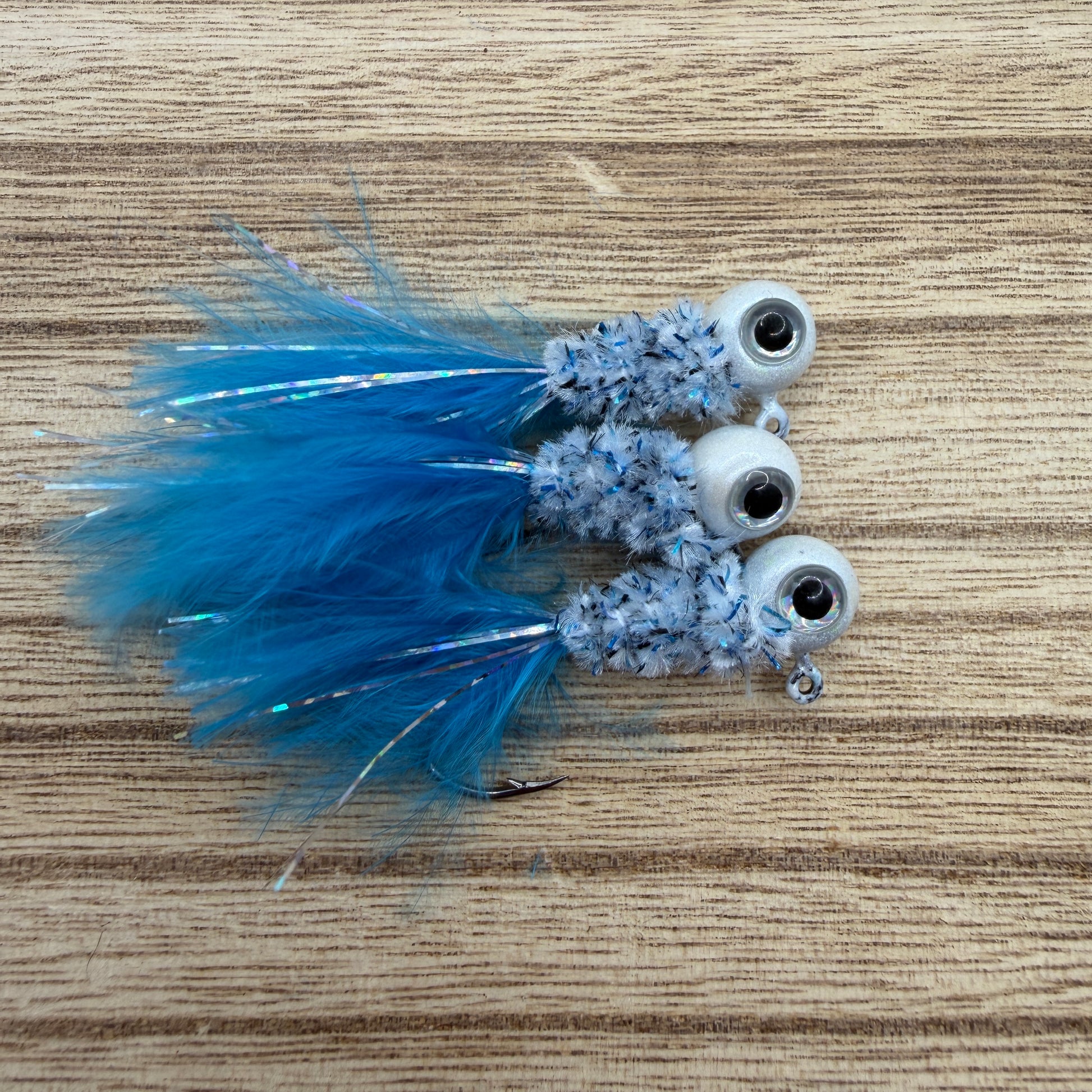 Three crappie fishing jigs with blue feathers and white beads on a wooden surface