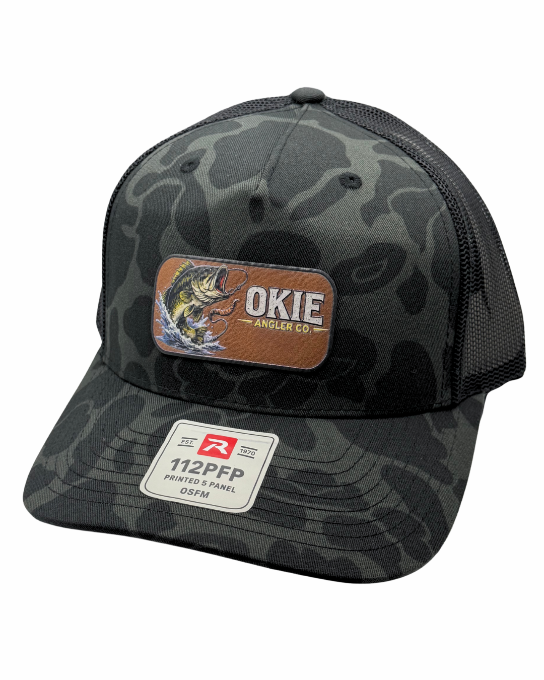 A dark gray and black camouflage trucker hat with a brown leather patch on the front that reads 'OKIE ANGLER CO' and features a white size patch on the brim.
