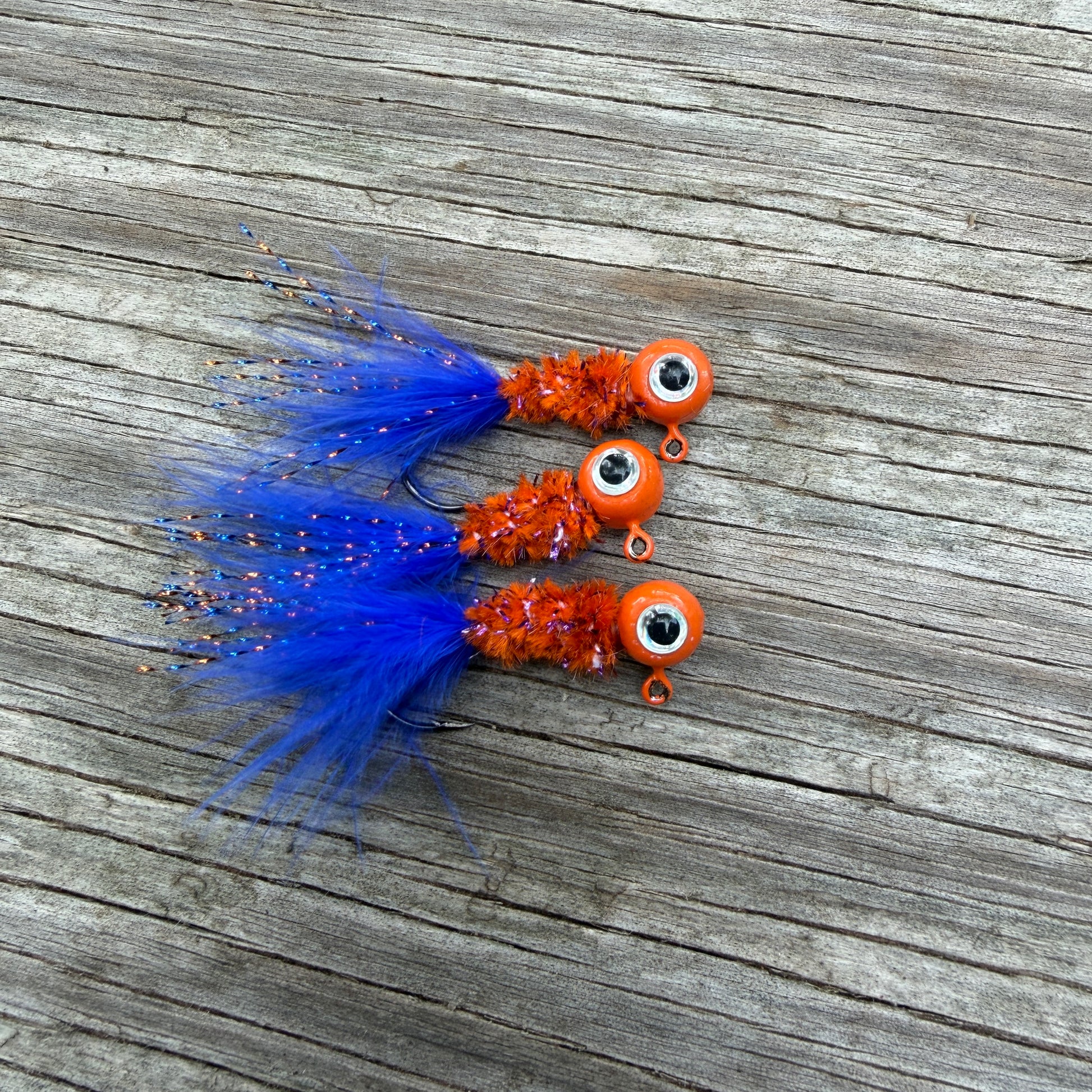 Three blue and orange crappie fishing jigs on a wooden surface.