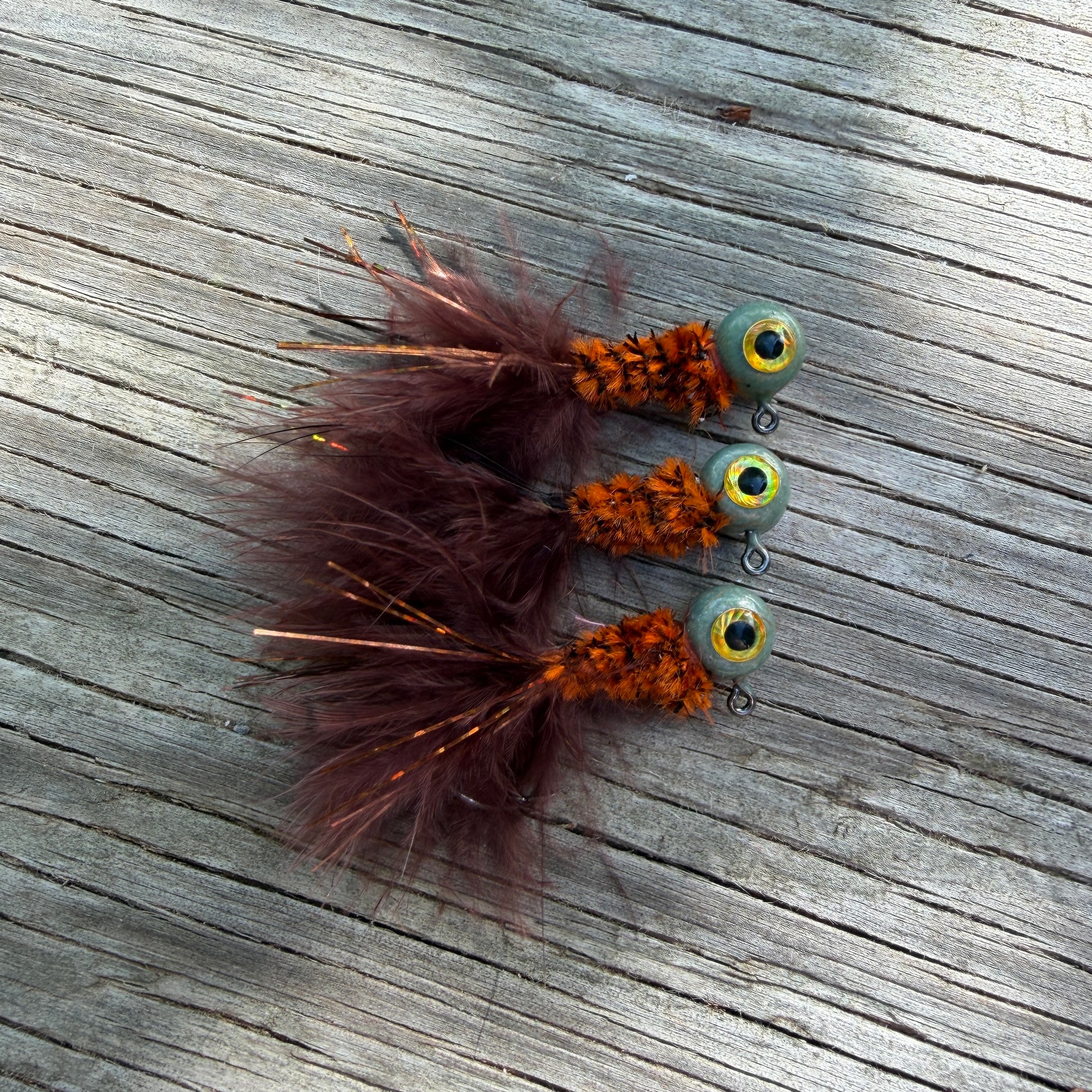 Three crappie fishing jigs with feathers on a wooden surface.